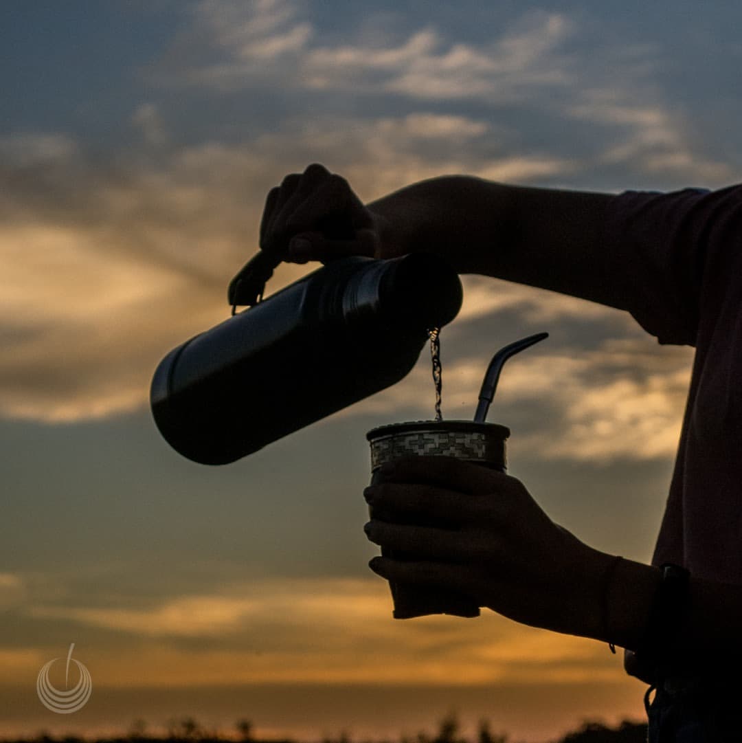Una persona sirve agua para preparar un mate junto al río